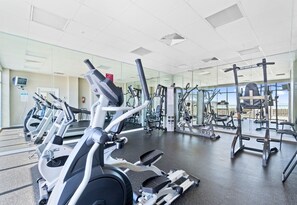 A gym with various exercise machines, a large mirror, and a view of the outdoors. - Beachfront Condo | Steps to Sand | 3 Pools (Navarre)