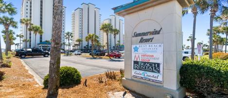 A sign for Summerwind Resort with a beach rental advertisement, palm trees, and tall buildings in the background.