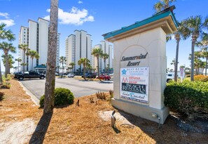 A sign for Summerwind Resort with a beach rental advertisement, palm trees, and tall buildings in the background.