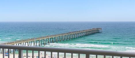 A beach with a pier extending into the ocean, a sandy beach with umbrellas, and a clear sky.