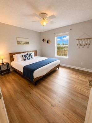 A bedroom with a bed, a ceiling fan, a window with a view, and a wall-mounted decoration. - 5 Min to beach + walk to zoo • sleeps 12 (Panama City Beach)