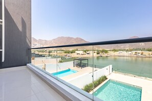 Uma varanda com piscina, vista para um corpo de água e montanhas ao longe.