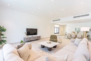 Uma sala de estar moderna com sofá, mesa de centro, TV e área de jantar.