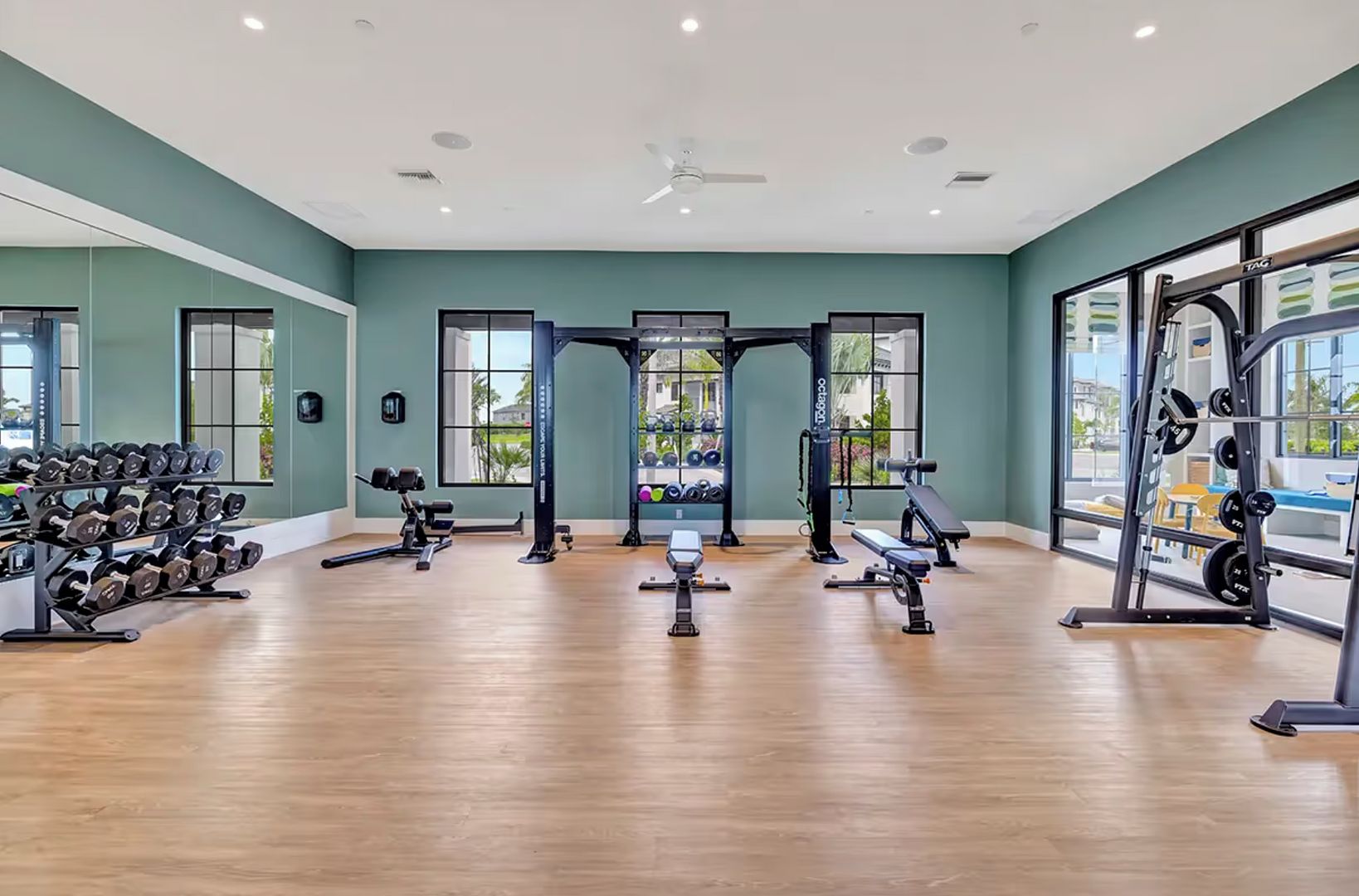Un gimnasio amplio con diverso equipo de ejercicio, ventanas grandes y suelo de madera.