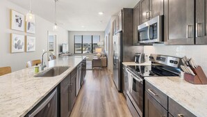 A modern kitchen with a central island, stainless steel appliances, and a view to the living area. - Landing Furnished Apartments - Port St. Lucie (Port Saint Lucie)