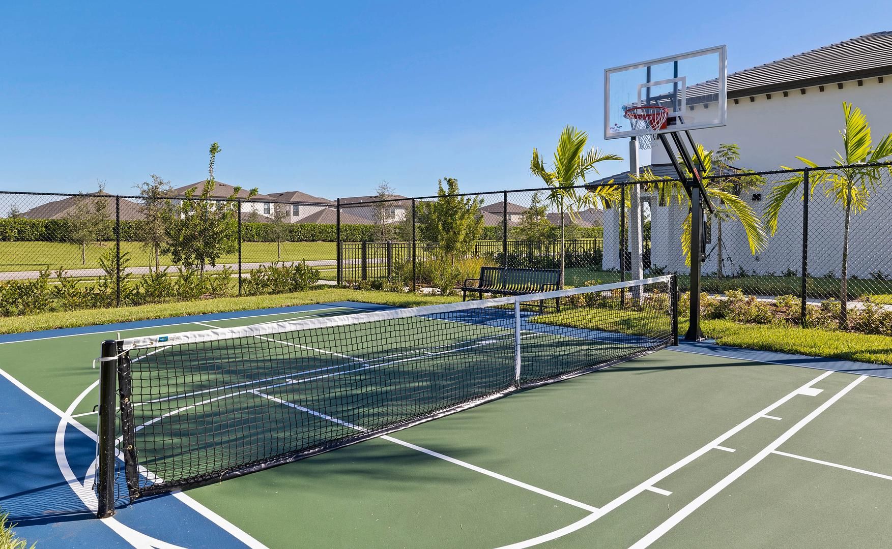 Un terrain de tennis avec un filet, un panier de basket et une clôture.