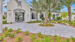 A building with a white facade, a number '11590' sign, and a paved courtyard with palm trees and benches. - Landing Furnished Apartments - Port St. Lucie (Port Saint Lucie)