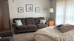 Een slaapkamer met een slaapbank, een bed, een nachtkastje en ingelijste foto's aan de muur.