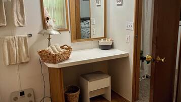 A bathroom with a wooden vanity, a mirror, a towel rack, a scale, and a shower area.