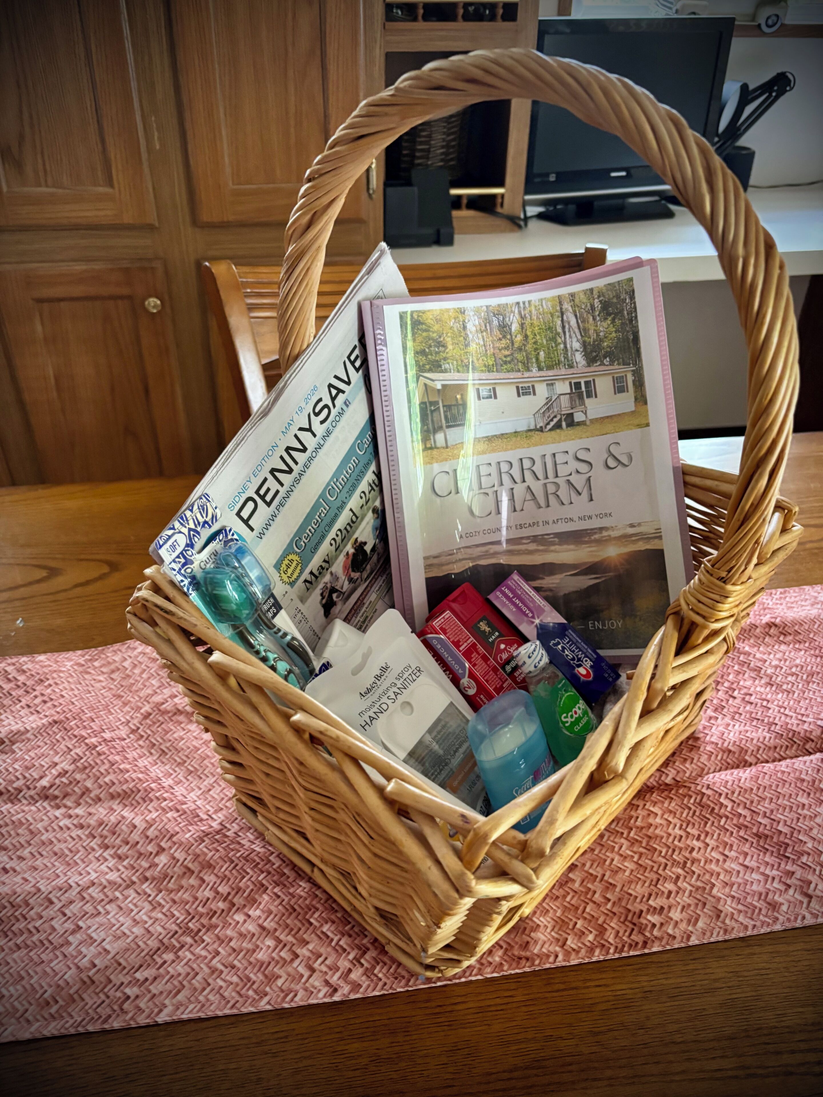 Una cesta de mimbre con revistas, gel antibacterial y un libro titulado 'Cherries & Farm'.