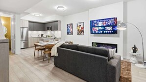 Uma sala de estar moderna com um sofá cinzento, mesa de jantar e cozinha ao fundo.