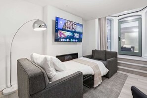 Habitació d'hotel moderna amb un llit, dues butaques, un televisor fixat a la paret i una porta corredissa de vidre que dona a un balcó.