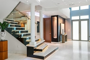 A modern interior with a glass staircase, a wooden door, and a large window.