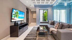 A modern living room with a flat-screen TV, a dark wooden entertainment unit, a grey sofa, and a glass partition wall. - Luxe Grove Villa with private pool (Miami)