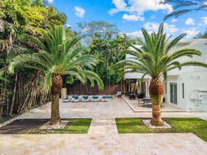 Un patio con dos palmeras, una piscina y mobiliario exterior.