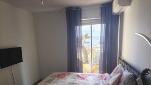 Une chambre à coucher avec un lit, une télévision, une fenêtre avec des rideaux et un appareil de climatisation.