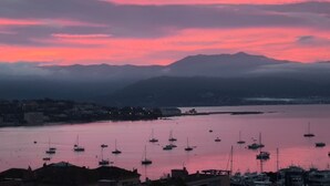 Un port de plaisance sur la côte, avec des bateaux, une ville au premier plan et des montagnes en arrière-plan.