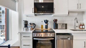 A modern kitchen with stainless steel appliances, white cabinetry, and a window with a view of buildings outside. - The Mccaul Near Kensington Market & Chinatown (Toronto)