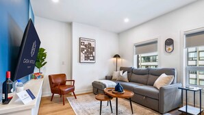 A modern living room with a grey sofa, a wooden coffee table, a brown leather chair, a flat-screen TV, and a framed abstract artwork on the wall. - The Mccaul Near Kensington Market & Chinatown (Toronto)
