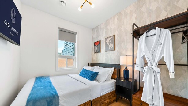 A hotel room with a bed, a window, a robe, and a nightstand. - The Mccaul Near Kensington Market & Chinatown (Toronto)