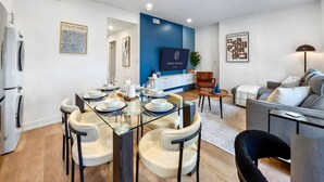 A modern hotel room with a dining area, a sofa, and a TV mounted on a blue accent wall. - The Mccaul Near Kensington Market & Chinatown (Toronto)