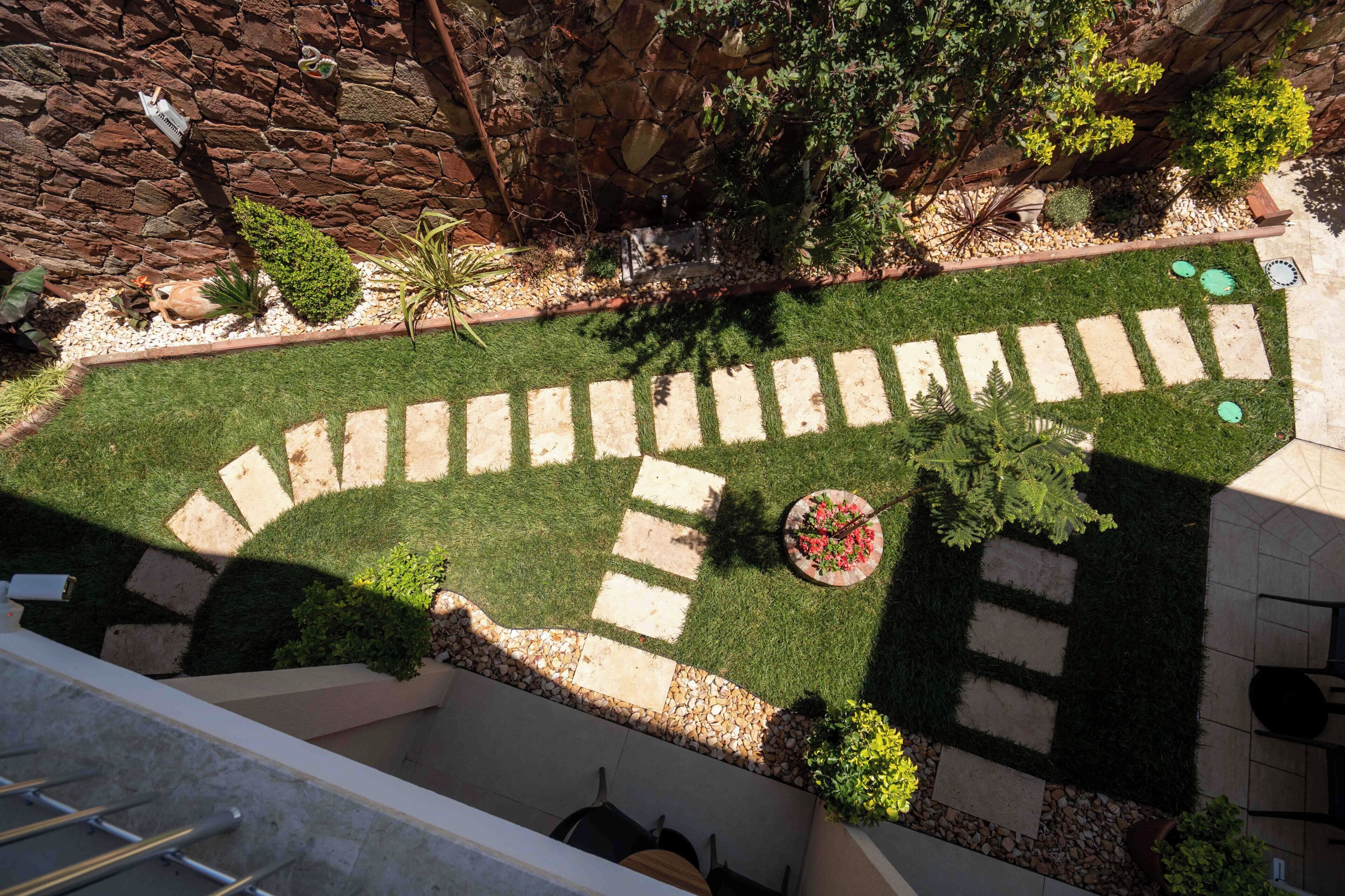 Un jardín en la azotea con un muro de piedra, un camino y diversas plantas.