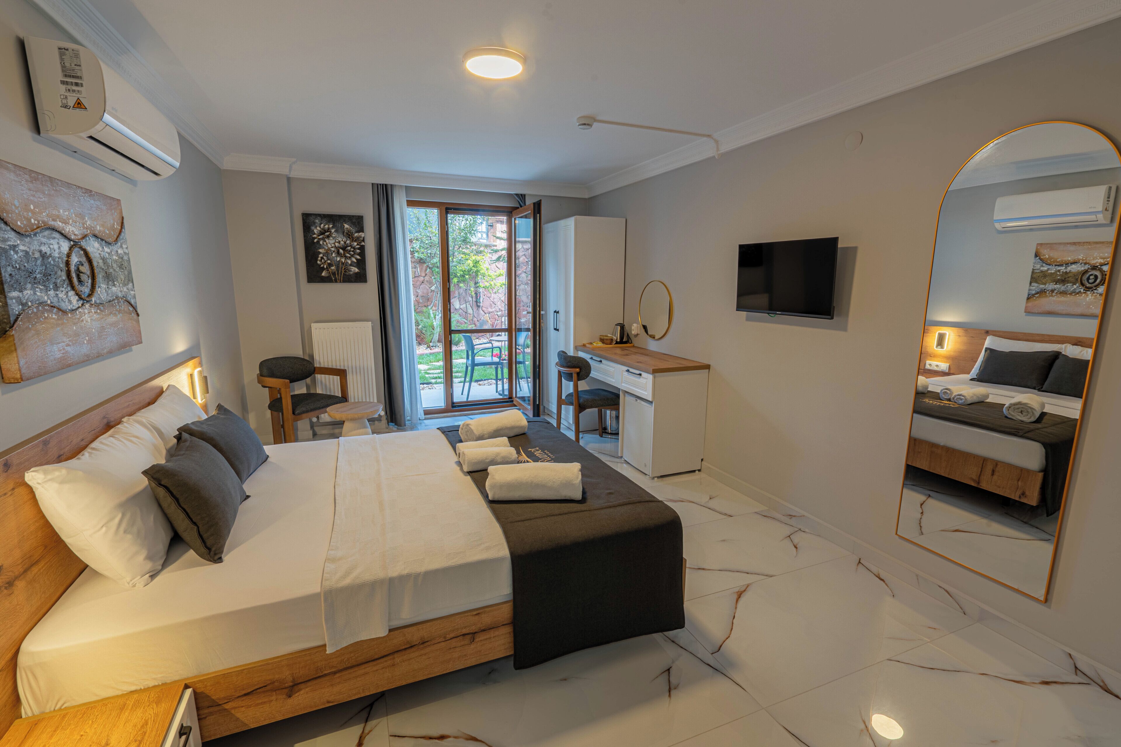 A modern hotel room with a large bed, a desk, a chair, and a TV.