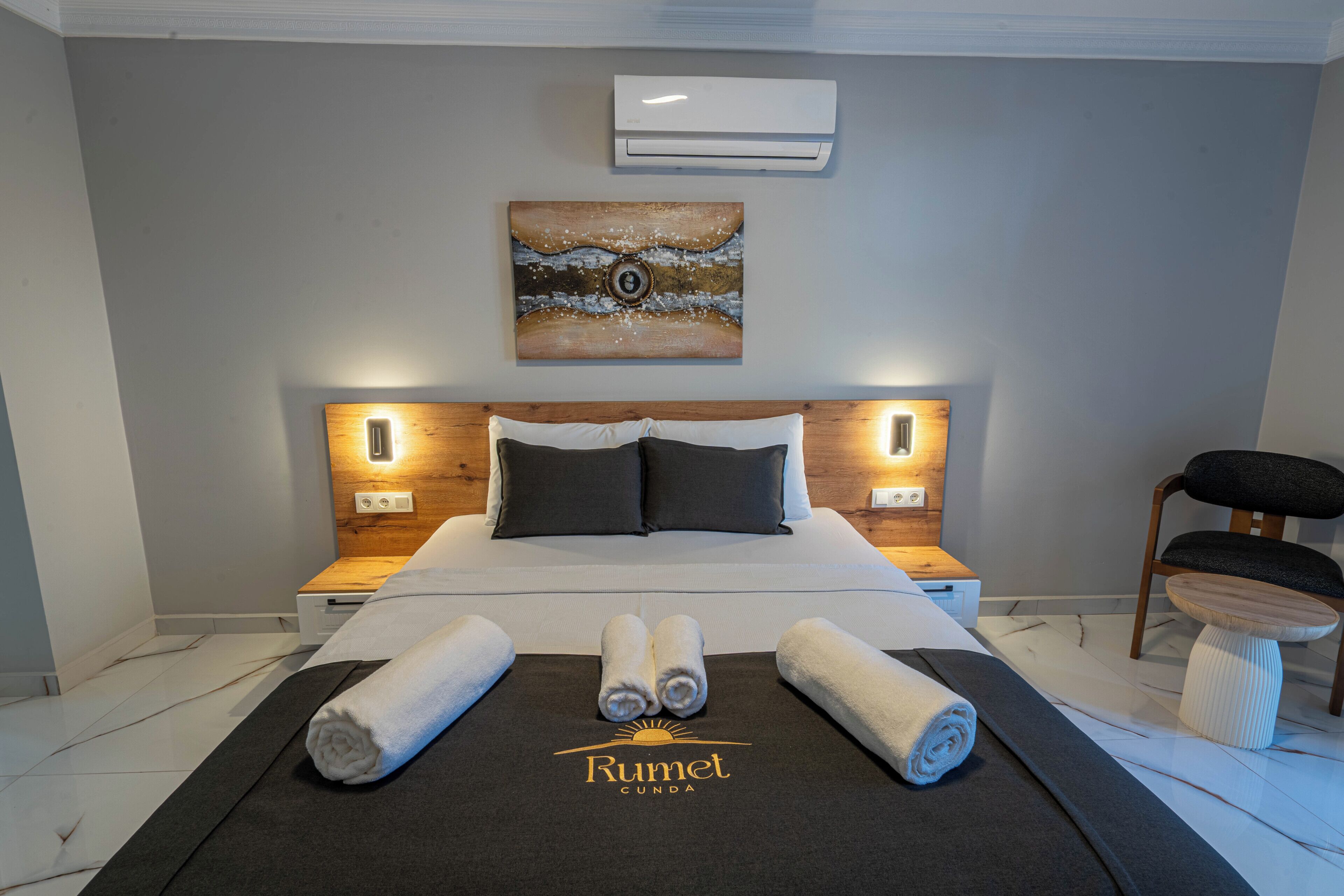 Une chambre d’hôtel avec un lit, deux tables de chevet, un climatiseur, un tableau et une chaise.