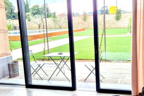 A room with a sliding glass door leading to an outdoor patio with a table and chairs. - Elegant Suite With Shared Pool (Adro)