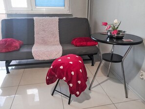 Ein moderner Wohnraum mit einem grauen Sofa, einem kleinen runden Tisch und einem roten Hocker mit Punkten.