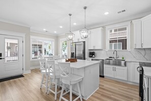 A modern kitchen with white cabinetry, a central island with bar stools, stainless steel appliances, and pendant lighting. - Ocean Lakes Site T37 - Beachside Blessings (Myrtle Beach)