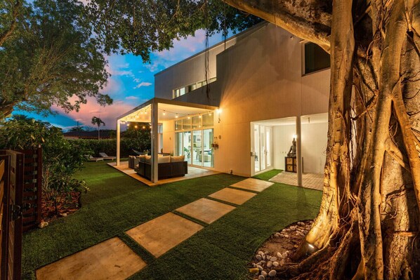 Une maison moderne dotée d’un patio couvert, d’une statue et d’une pelouse bien entretenue.