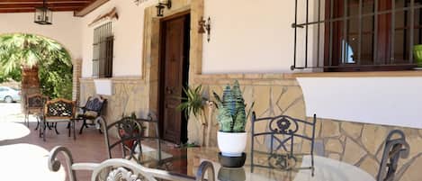An outdoor seating area with a glass table and metal chairs, a potted plant, and a stone wall.