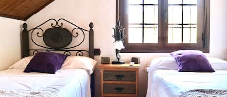 Ein Zimmer mit zwei Betten, einem Nachttisch, einer Lampe und einem Fenster.