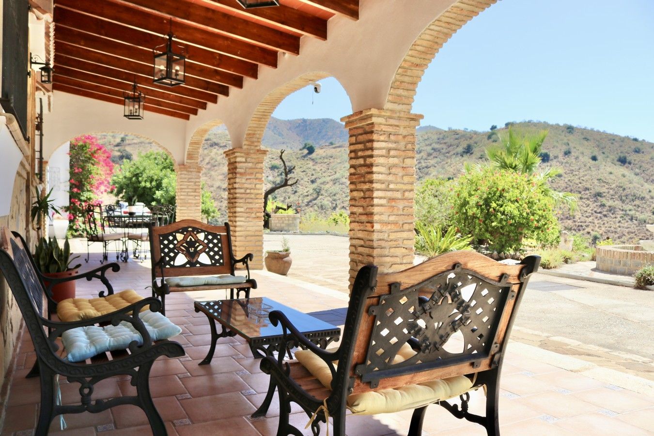 Un patio al aire libre con columnas de ladrillo, bancos de madera y plantas en macetas.