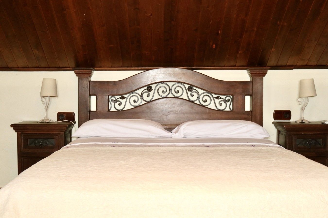 A bed with a wooden headboard, two bedside tables with lamps, and a plain wall.
