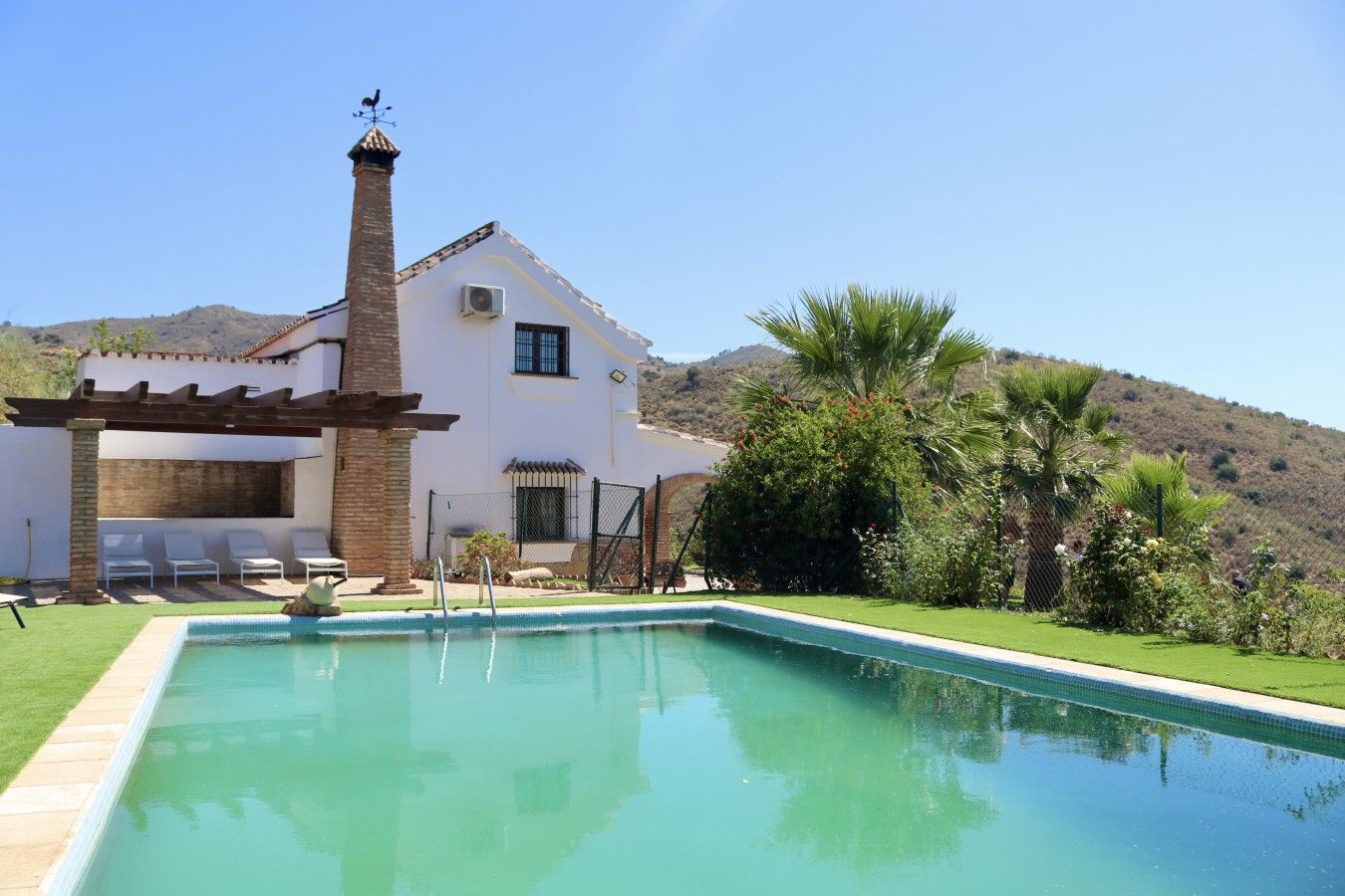 A house with a swimming pool, a pergola, and a view of a hill.
