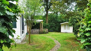 A garden pathway leading to a white building with a covered area, surrounded by lush greenery. - Vechtdal Chalet de Eik (Rheezerveen)