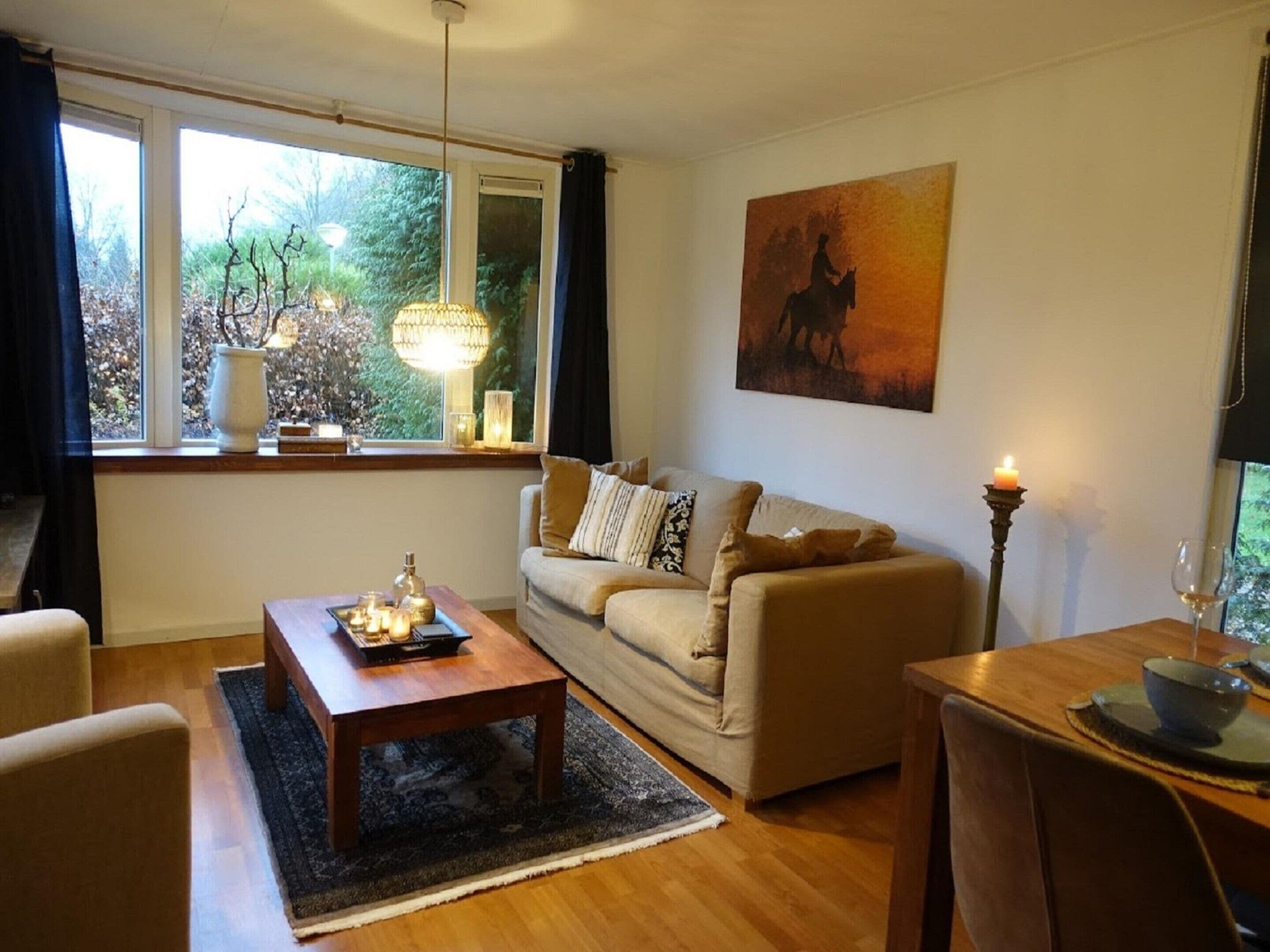 A living room with a sofa, a coffee table, a dining table with a candle, and a painting on the wall.