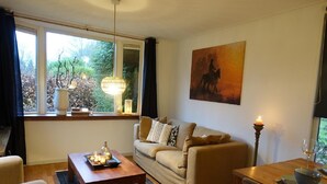 A living room with a sofa, a coffee table, a dining table with a candle, and a painting on the wall. - Vechtdal Chalet de Eik (Rheezerveen)