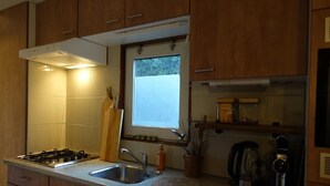A kitchen with wooden cabinets, a gas stove, a sink, a window, and a coffee maker. - Vechtdal Chalet de Eik (Rheezerveen)