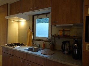 Una cocina con armarios de madera, estufa a gas, lavaplatos, ventana y cafetera.