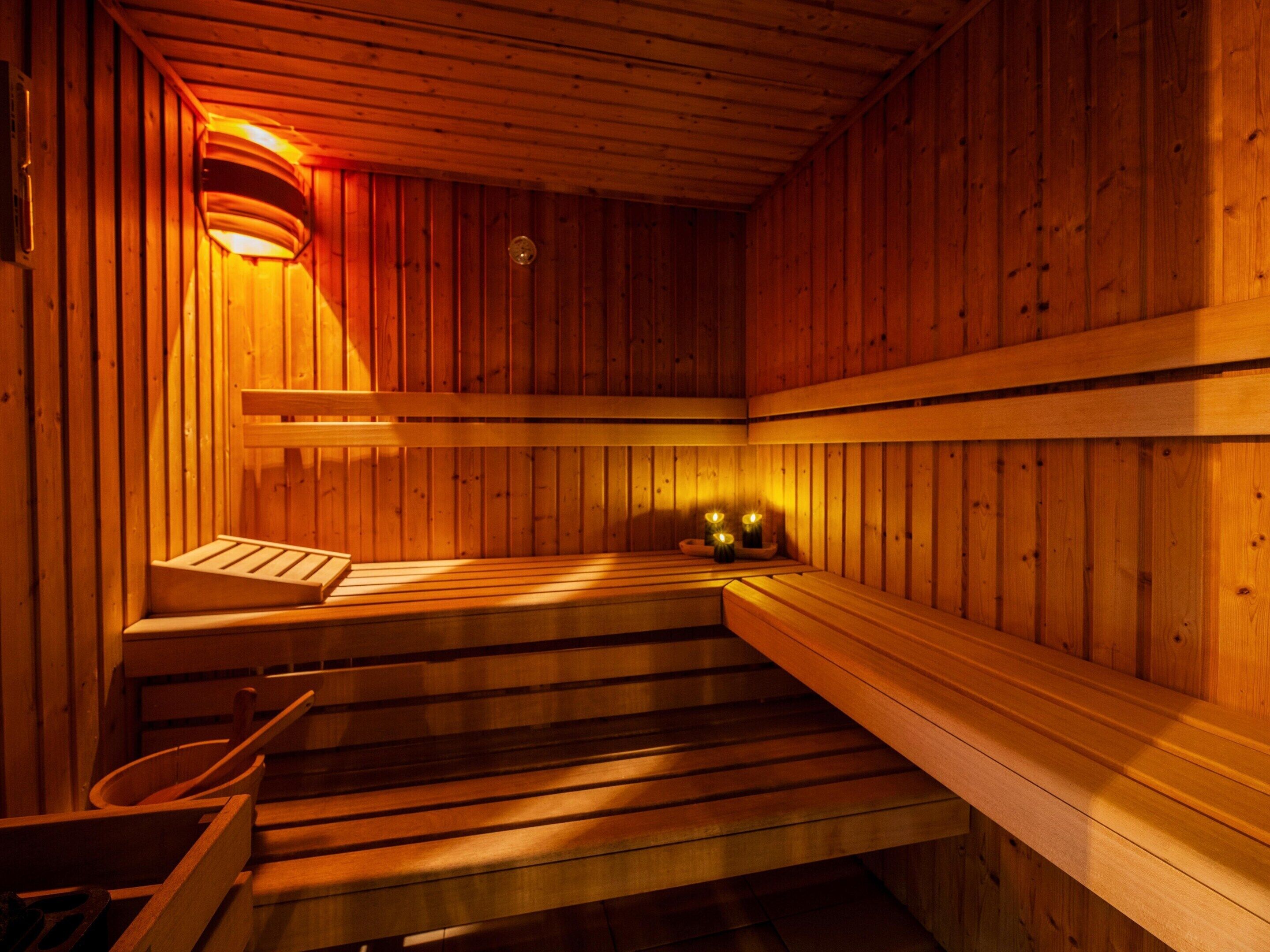 A sauna with wooden benches and walls, a bench with a towel, and a light fixture on the wall.