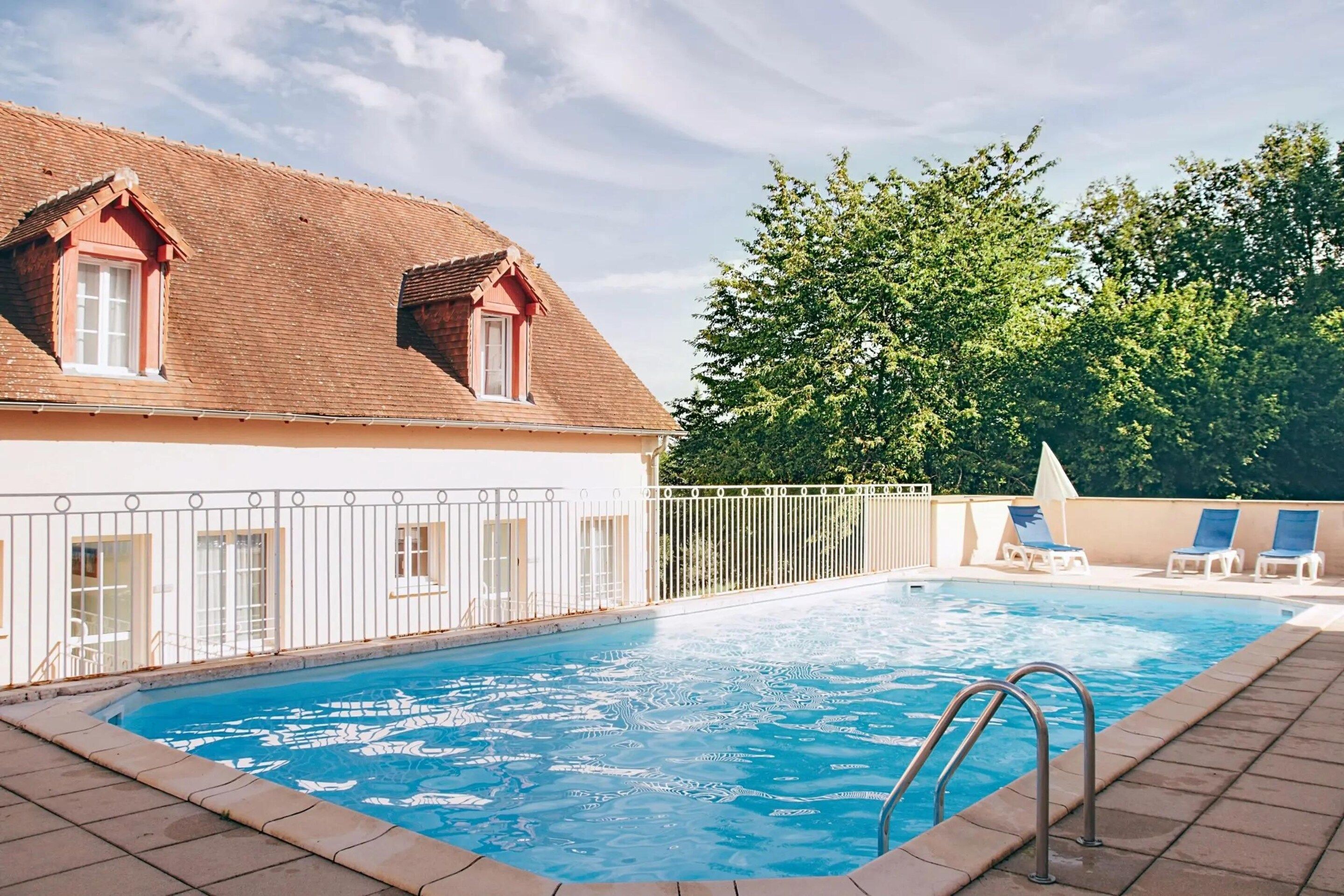 A swimming pool with a tiled deck, a metal ladder, and a white fence.