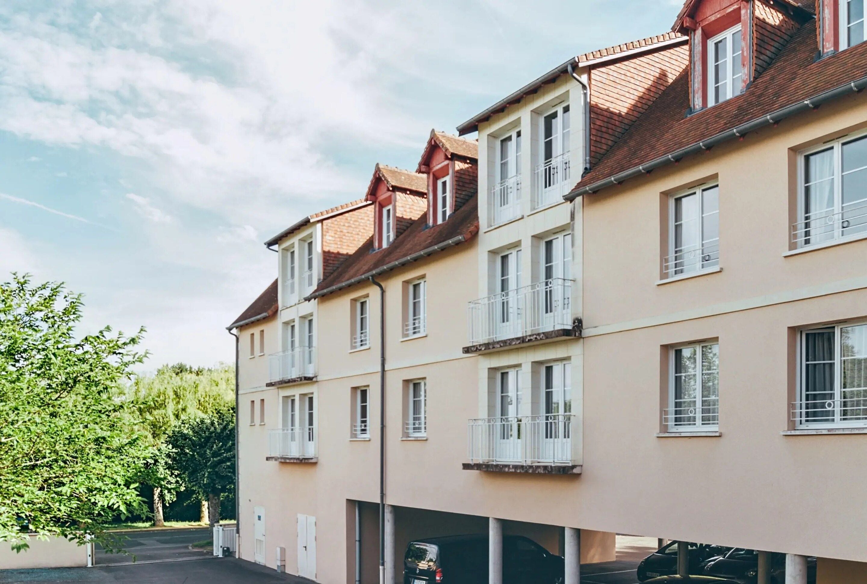 A multi-story residential building with balconies, a parking garage, and a clear sky.