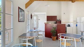 A modern kitchen with wooden beams, a dining area with tables and chairs, and a view through large windows.