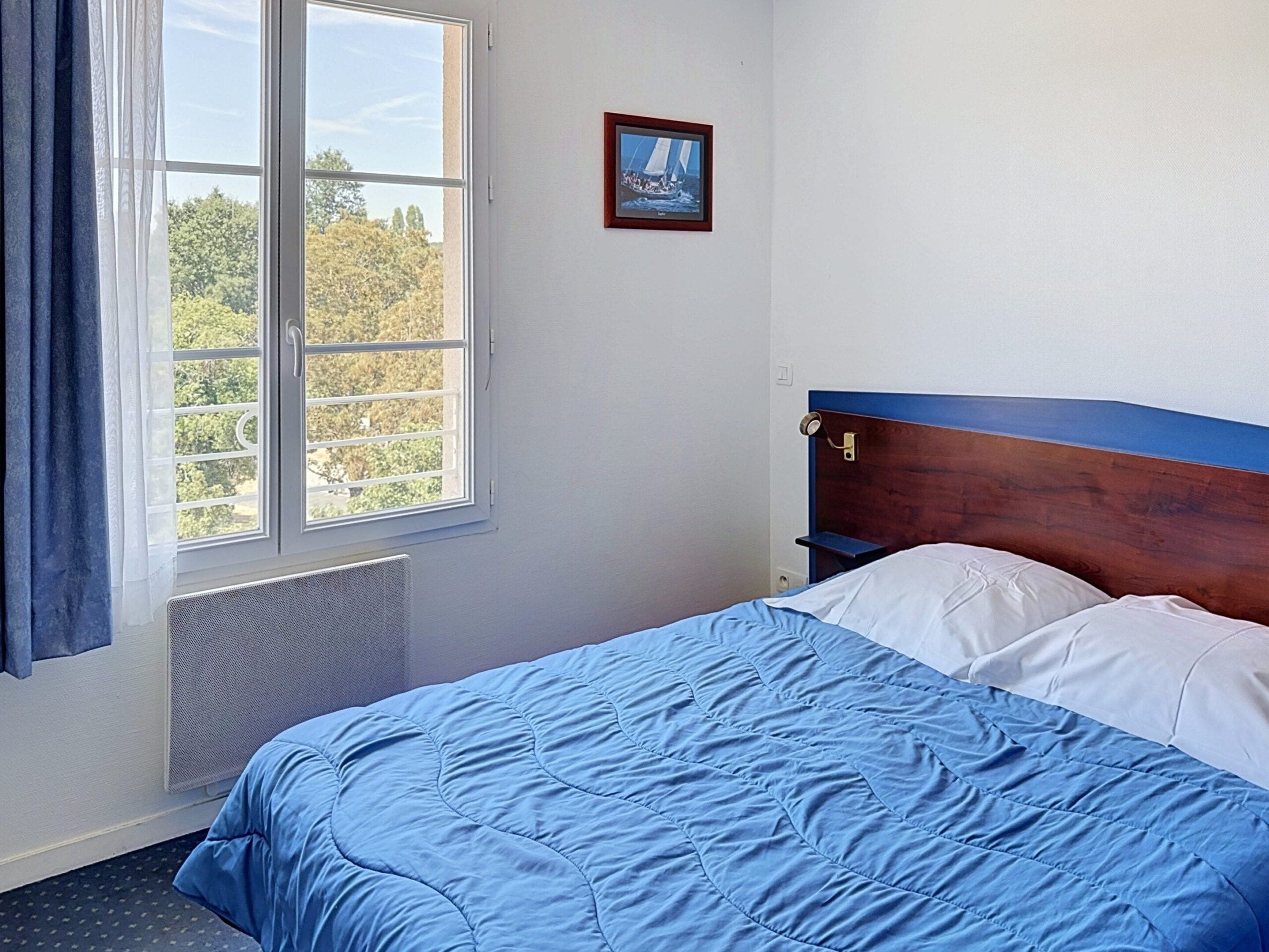 A bedroom with a bed, a window, a radiator, and a wall-mounted picture.