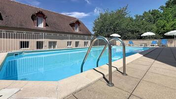 Una piscina con solárium empedrado, escaleras metálicas y sillas de descanso con sombrillas.