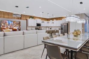 A modern kitchen with white cabinets, a dining area with a glass table, and a living room with a large window. - 10BR house with game room, sleeps 22 in clermont (Clermont)