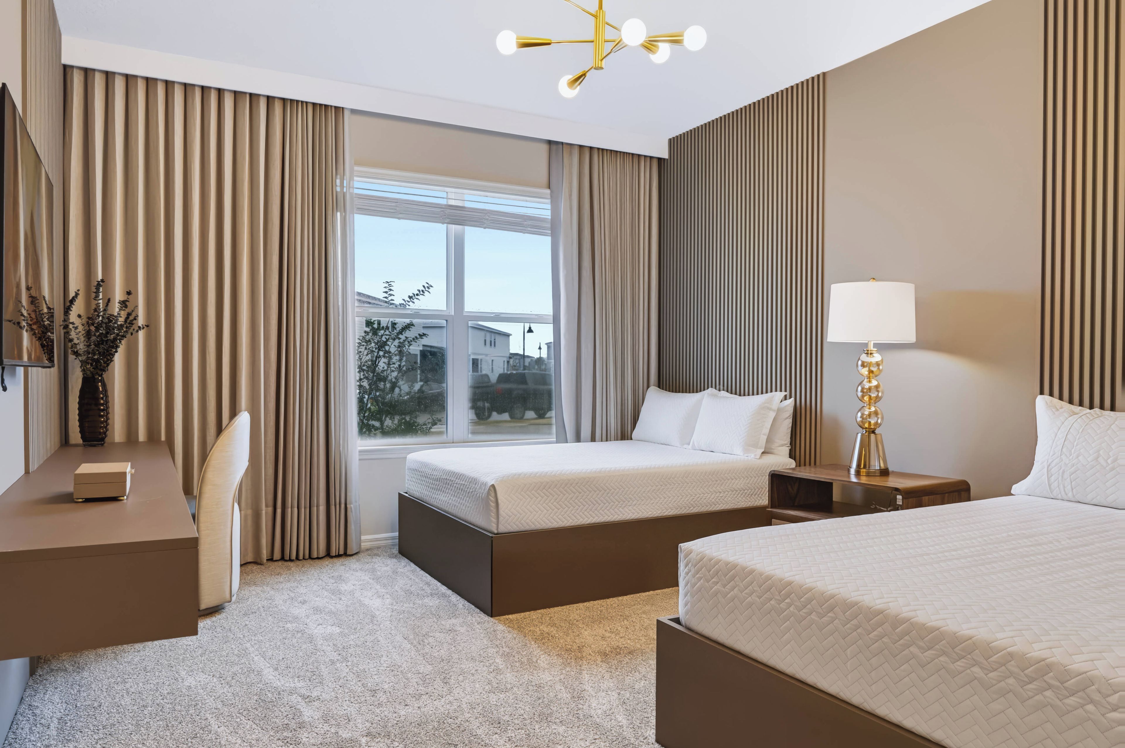 Ein Hotelzimmer mit zwei Betten, einem Schreibtisch, einer Lampe und Blick nach draußen.